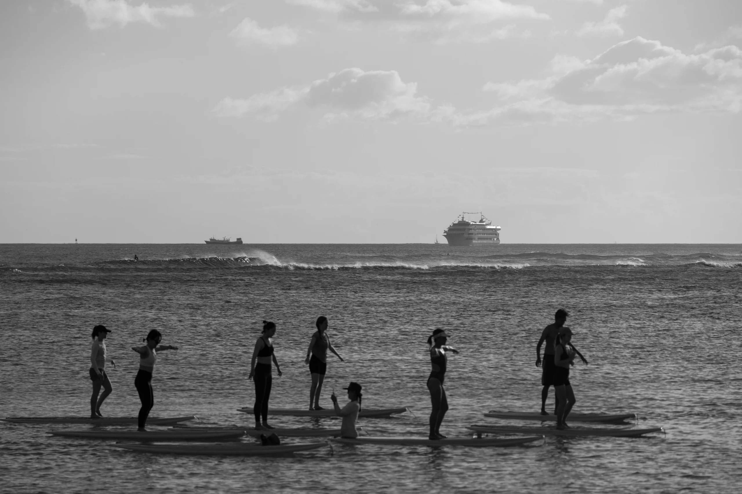 Silhouette of a group paddle boarding on the ocean with a distant cruise ship by Jess Loiterton, via Pexels. optimized